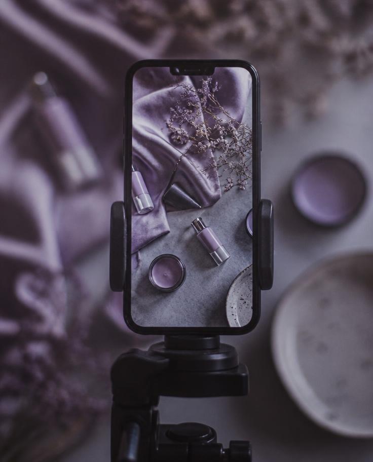 Phone on a tripod filming a violet-toned product flat lay